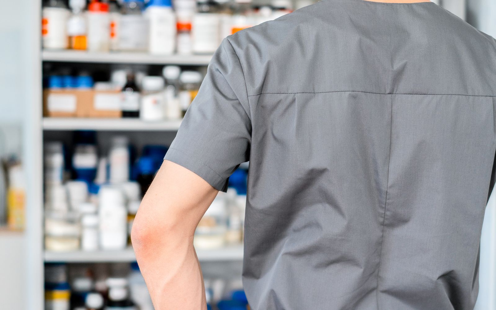 Profesional de espaldas organizando inventario en estanterías farmacéuticas